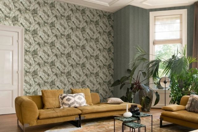 Wohnzimmer mit Blättertapete und goldfarbenem Sofa